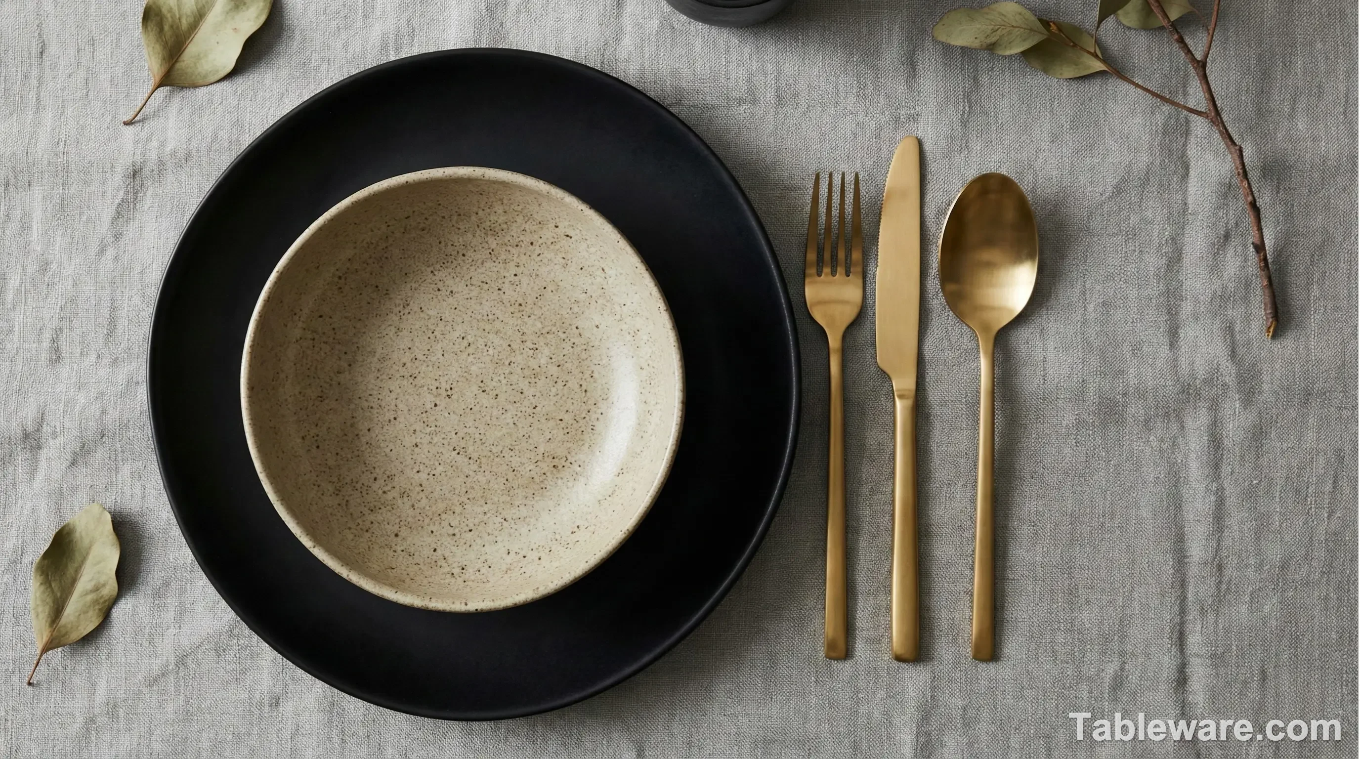 A top-down view of a dining table featuring a mix of terracotta dinner plates, oatmeal salad bowls, and gold matte flatware.