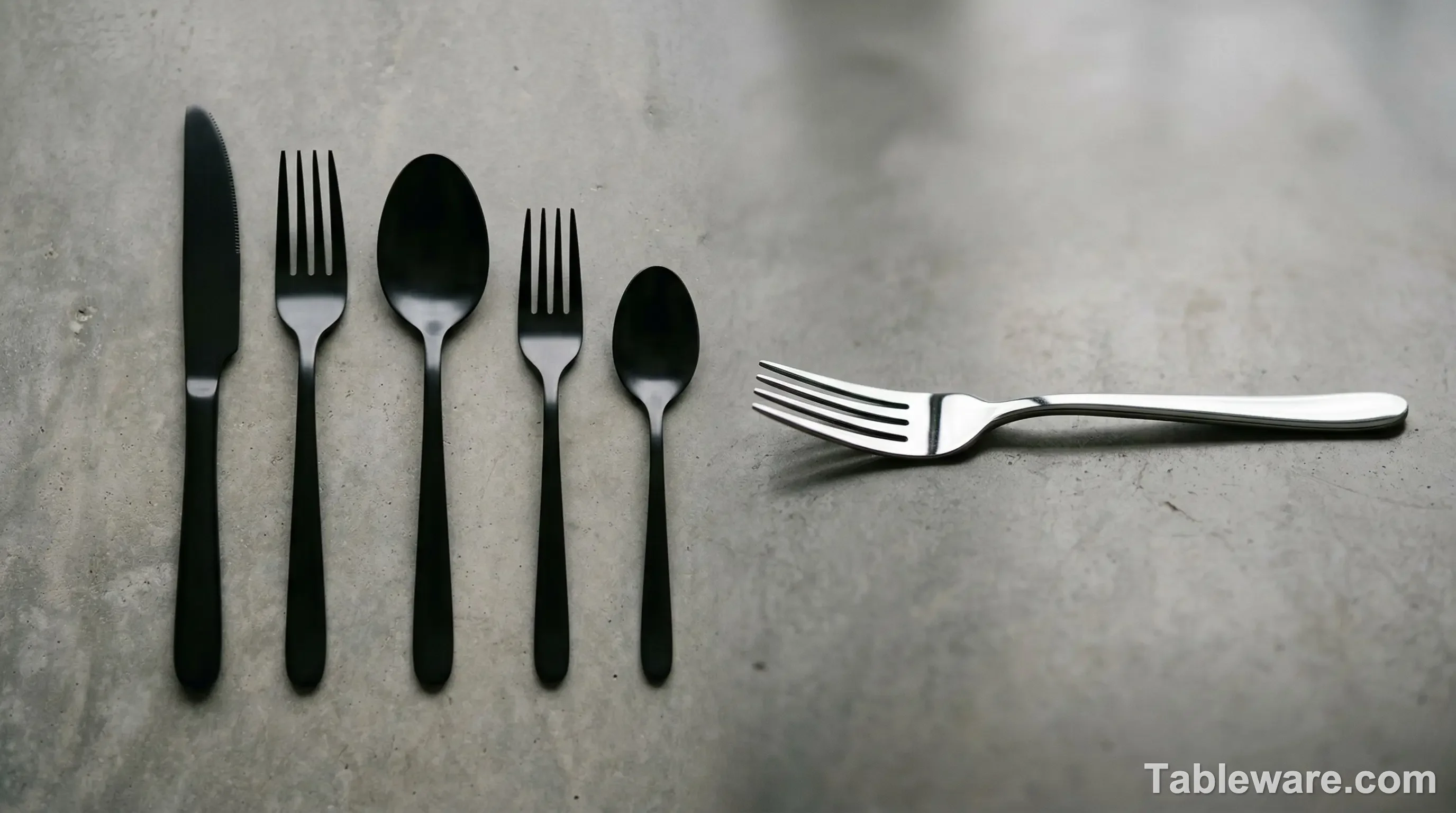 A minimalist product portrait comparing a complete five-piece matte black flatware set, neatly arranged, against a single, mirror-polished 18/10 stainless steel dinner fork placed horizontally, reflecting ambient light.