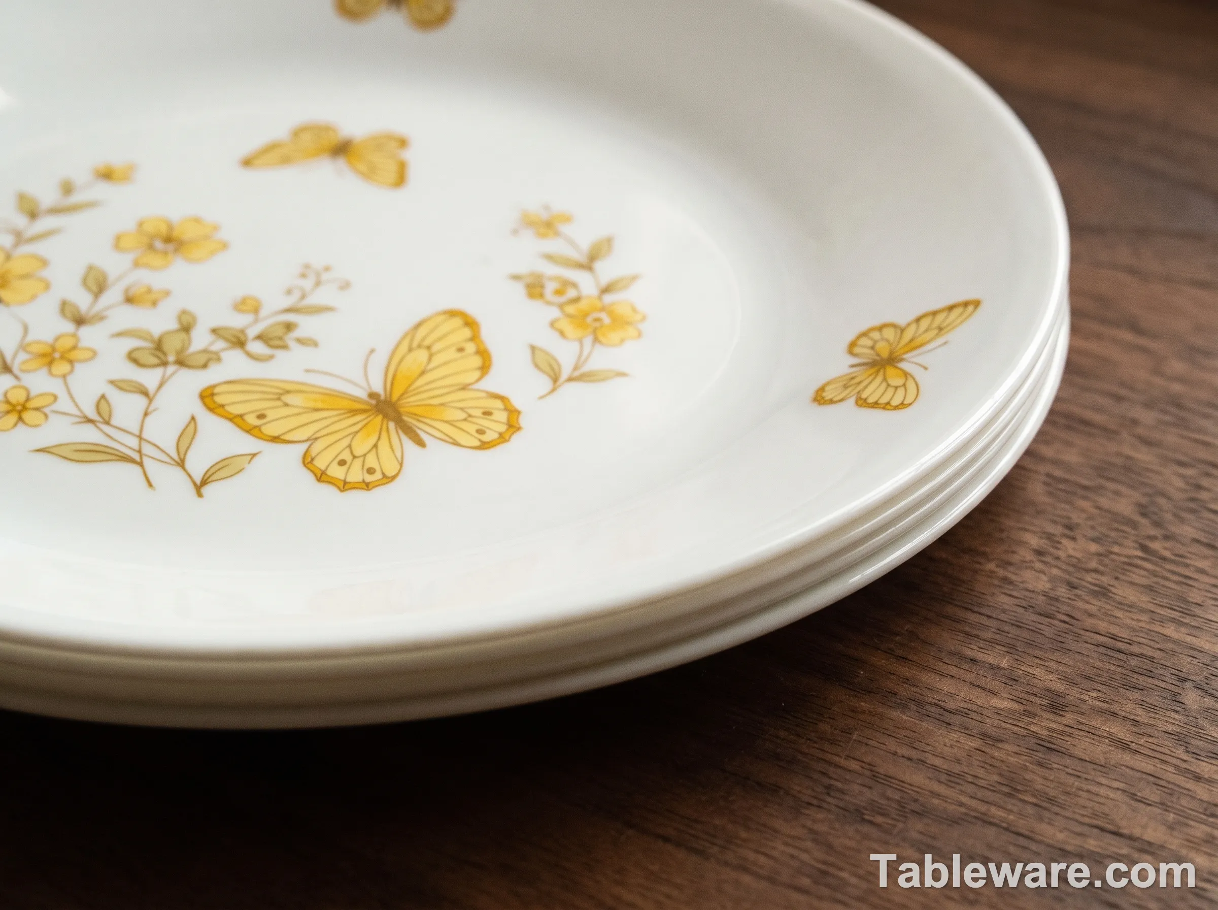 Close-up of a vintage 1970s Corelle Butterfly Gold plate, white Vitrelle glass with delicate yellow butterfly and floral motifs, sitting on a dark walnut table. Soft natural side lighting.